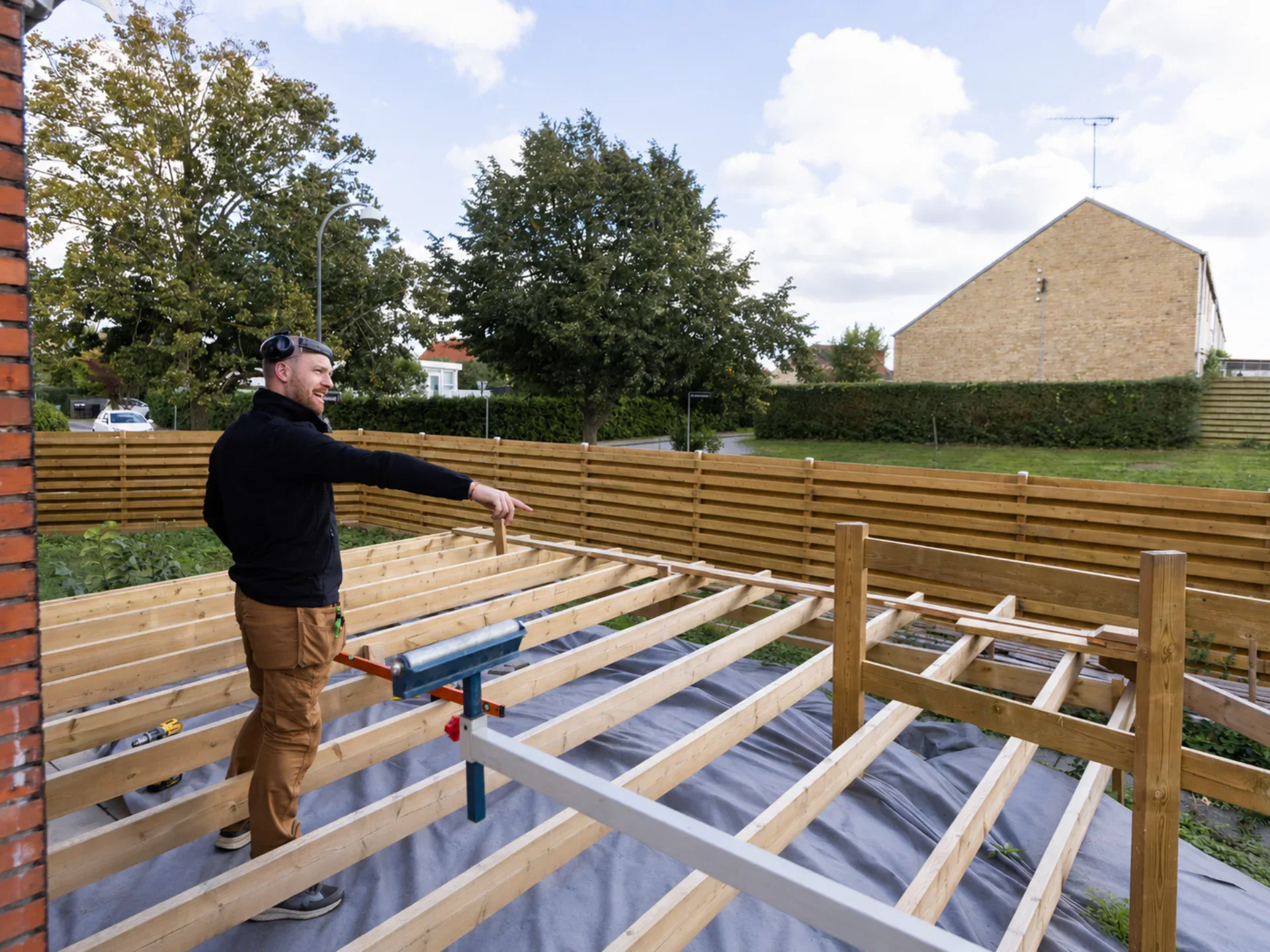 Tømrer arbejder på udendørs terrassekonstruktion i have.