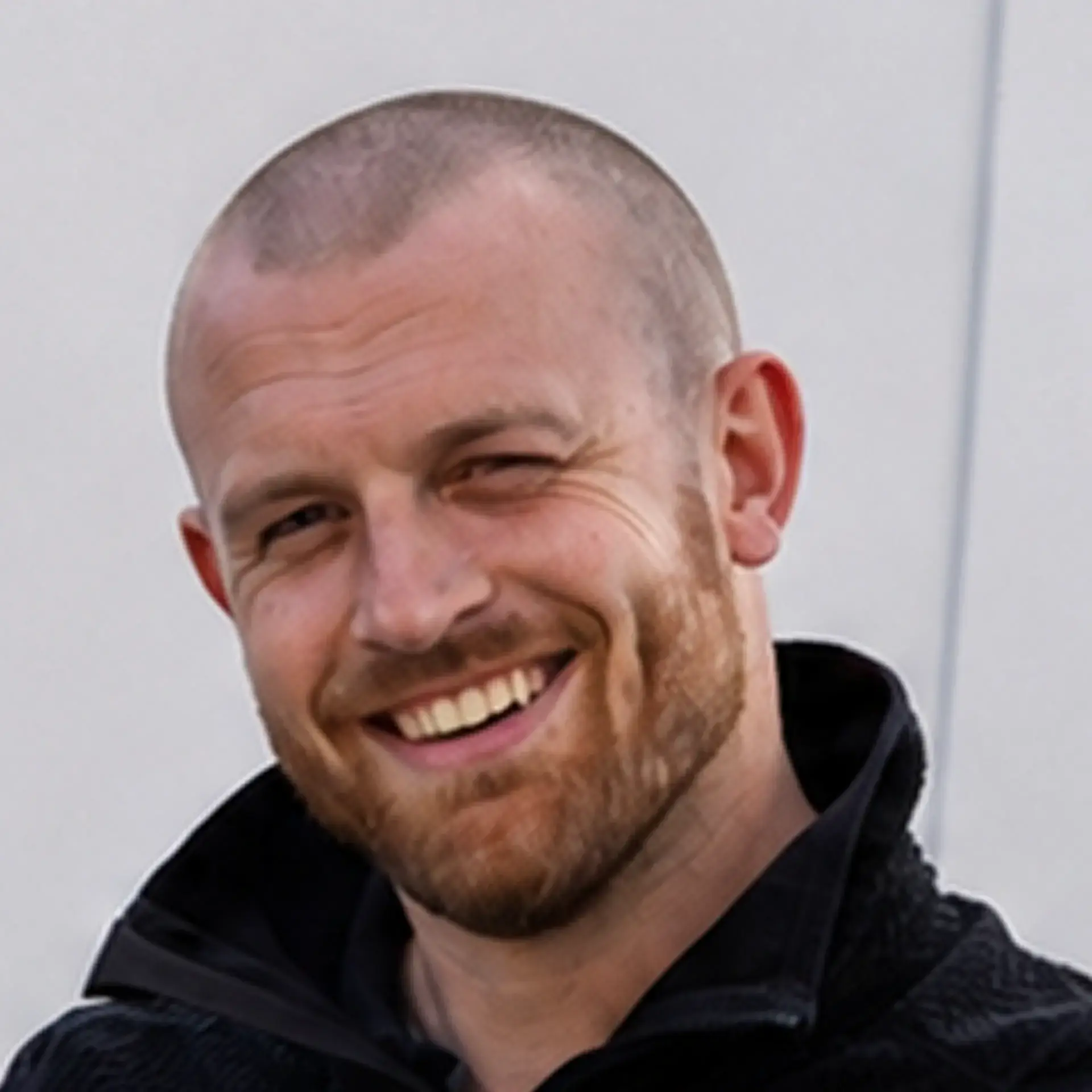Mand med kort hår og skæg smiler bredt mod kameraet.