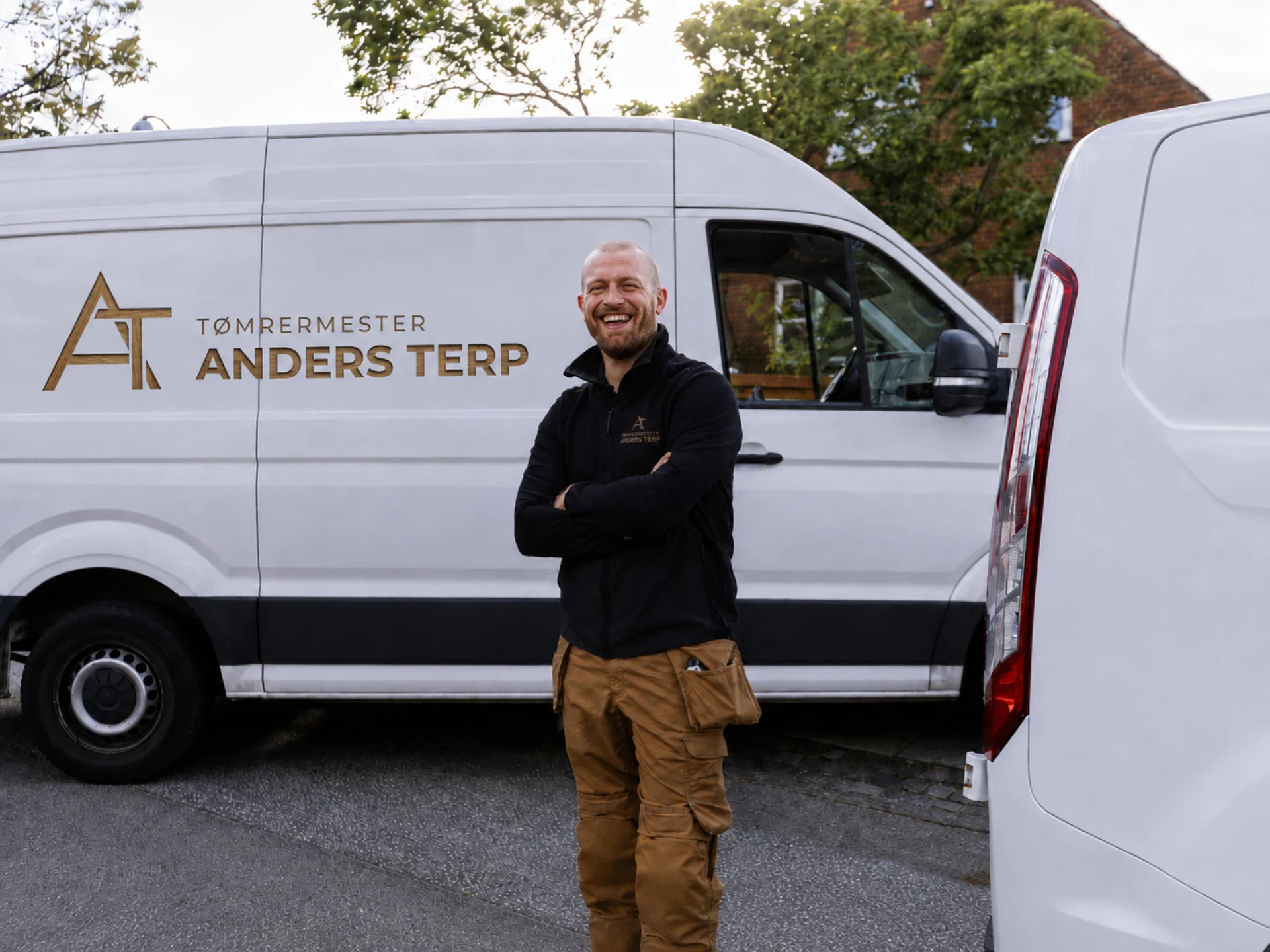 Tømrermester Anders Terp står foran firmaets varevogn med logo.