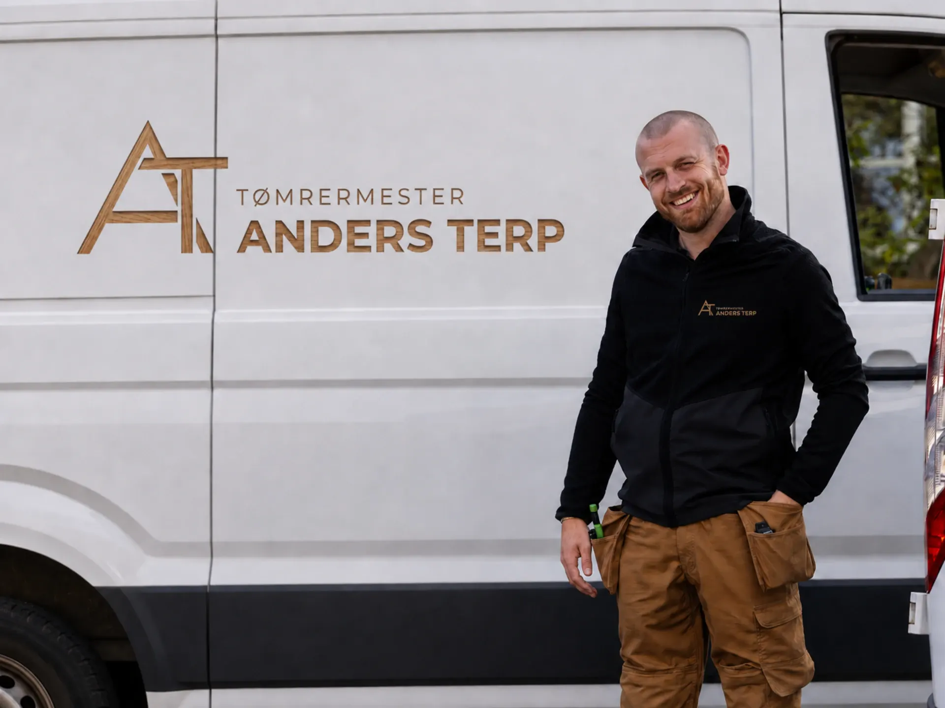 Tømrermester Anders Terp foran firmaets logo på firmabilen.