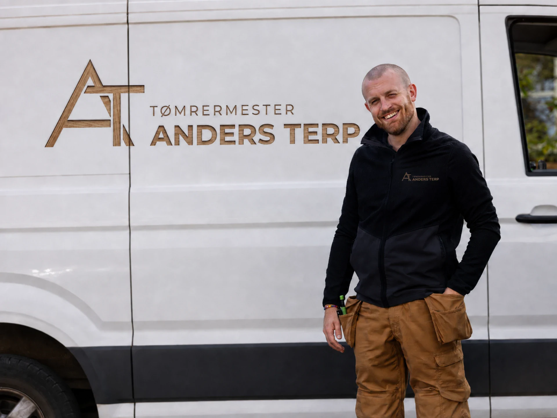 Tømrermester Anders Terp står foran firmaets varebil med logo.