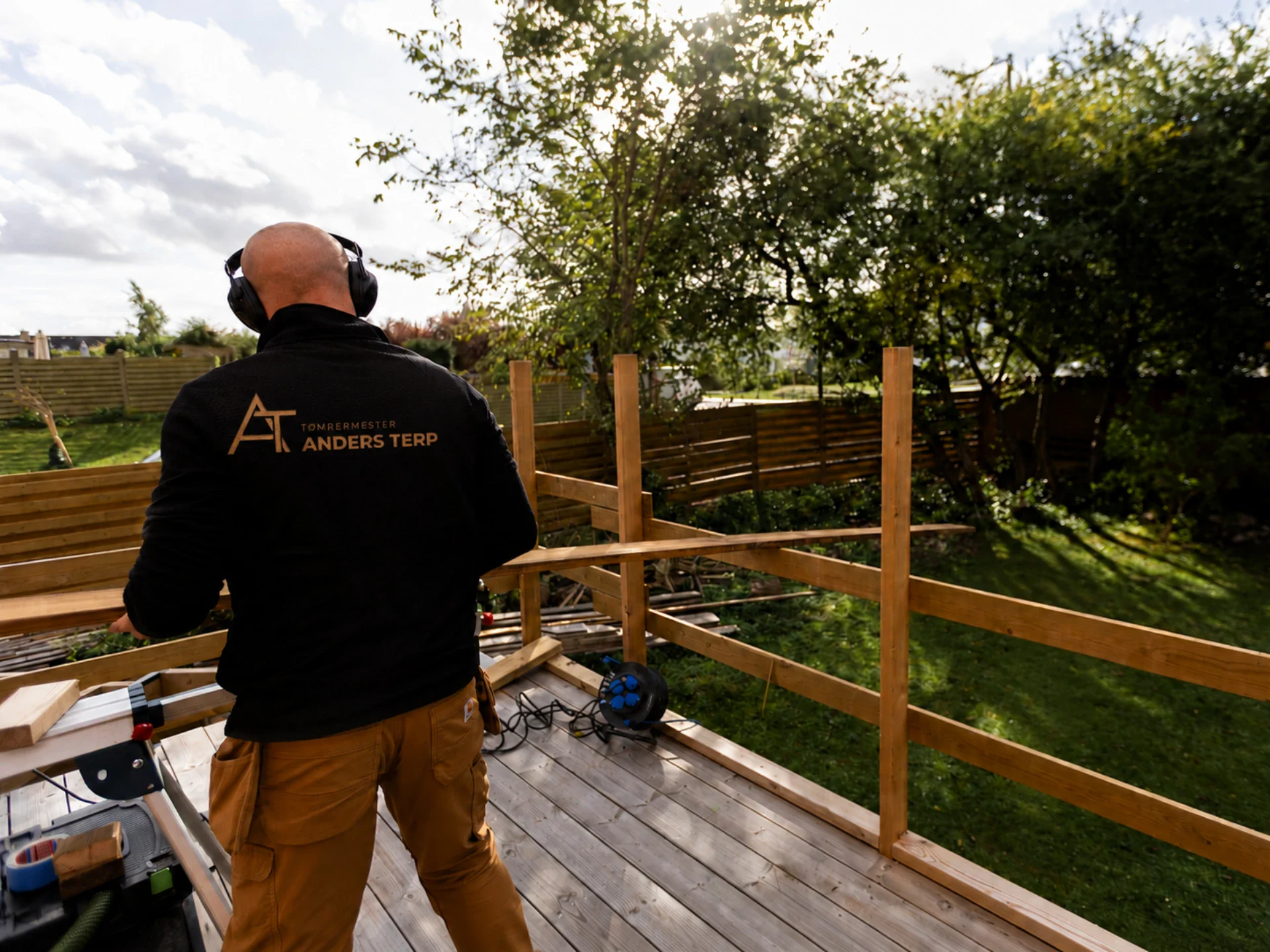 Tømrer arbejder på udendørs terrasse med træværk og værktøj.